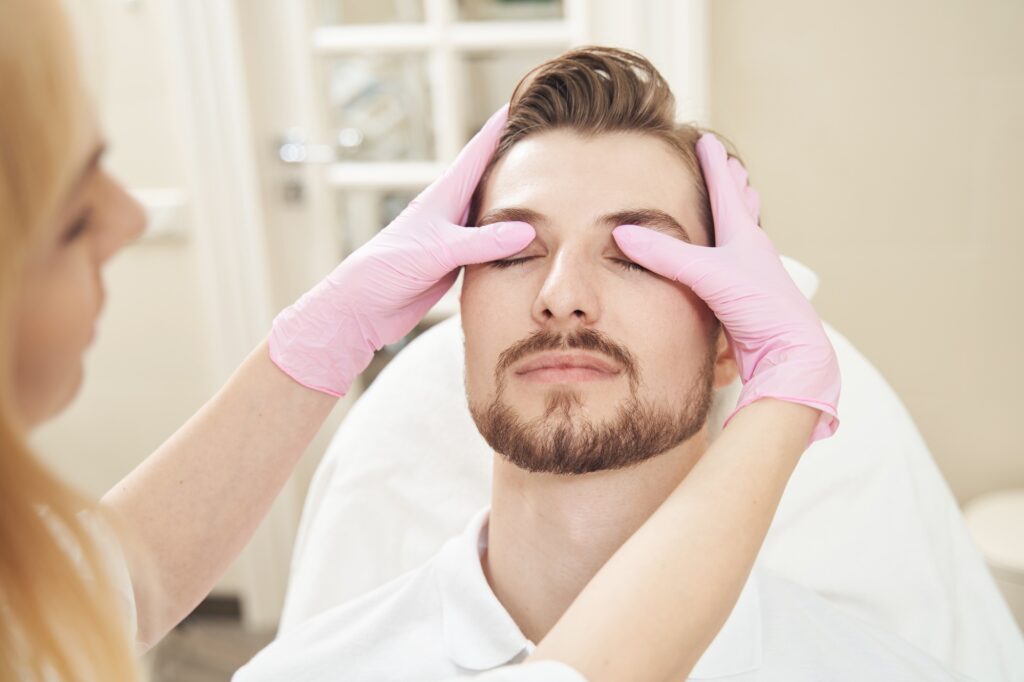 Cosmetologist examining patient eyelids and forehead in beauty shop